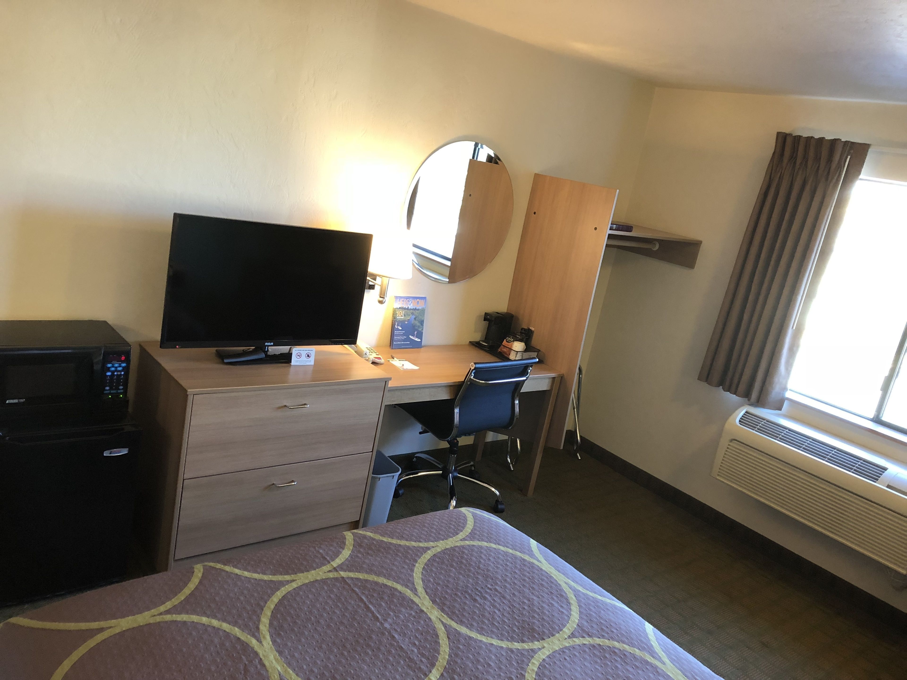 Una habitación de hotel con cama, escritorio con computadora, televisión, microondas y ventana con cortinas.