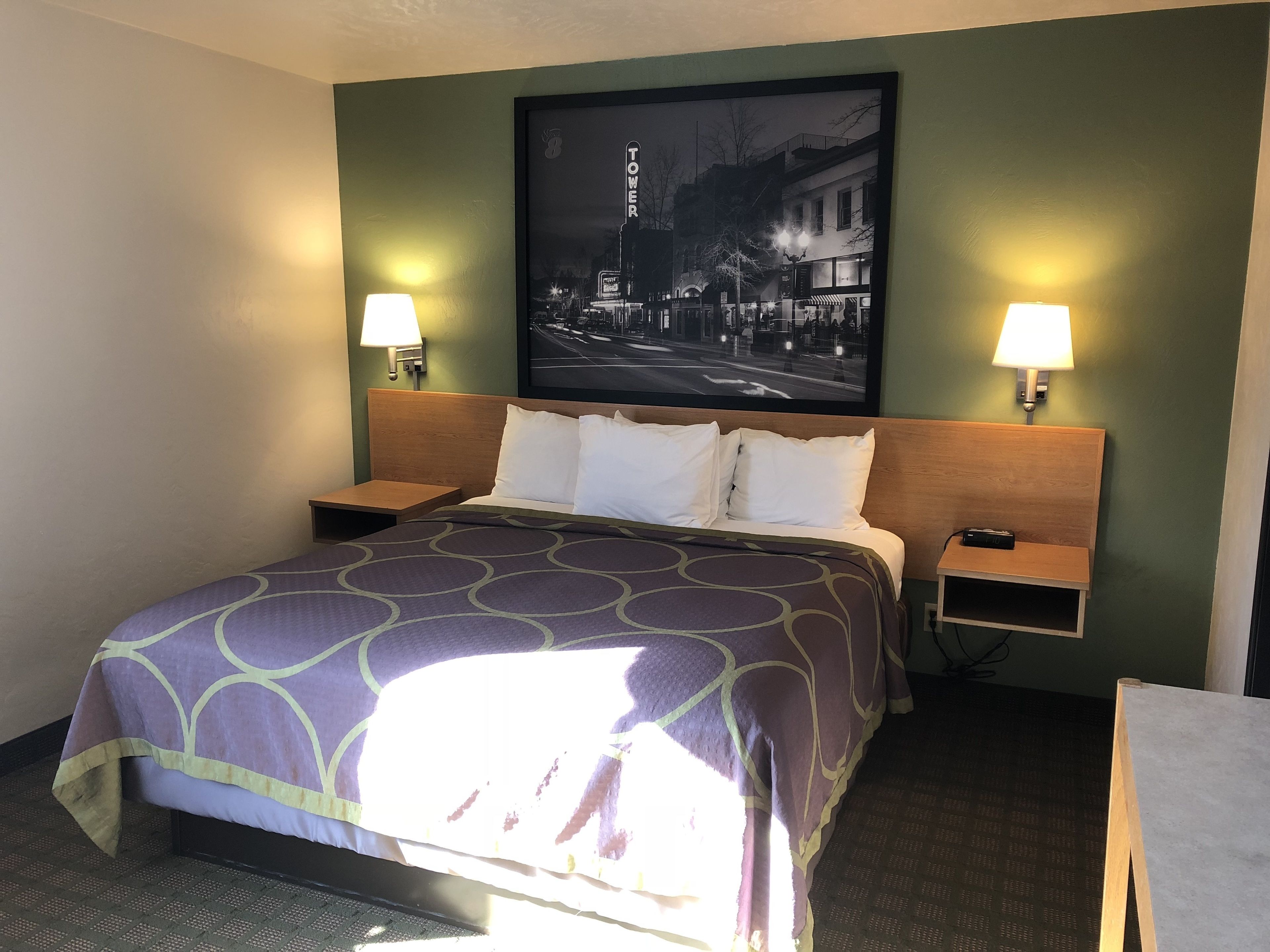 A hotel room with a bed, two bedside tables, a nightstand, a wall-mounted TV, and two wall lamps.