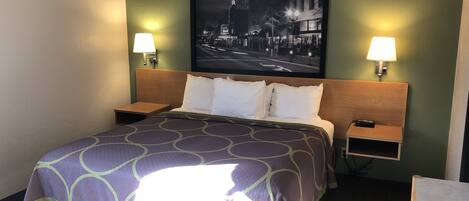 A hotel room with a bed, two bedside tables, a nightstand, a wall-mounted TV, and two wall lamps.
