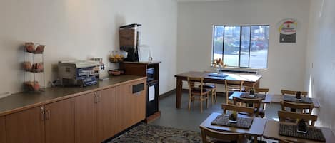 A dining area with wooden tables and chairs, a coffee machine, and a window with a view of the street.