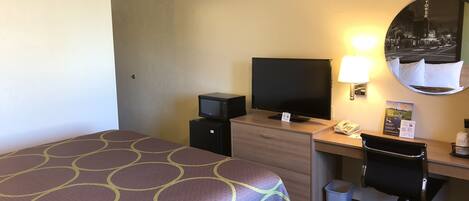 A hotel room with a bed, a desk with a computer, a television, a lamp, and a mirror.