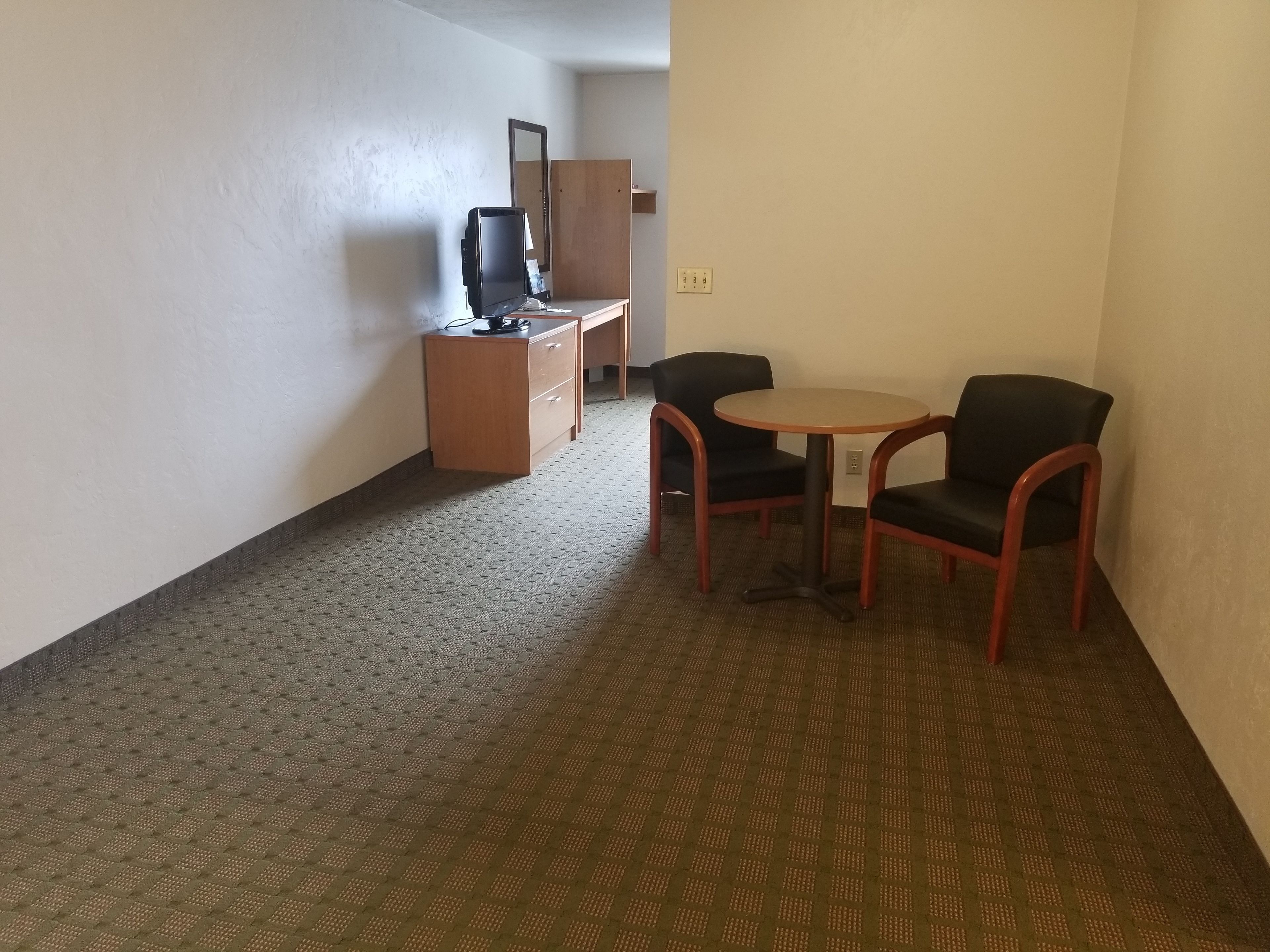A hotel room with a small desk, a chair, a round table, and a television.