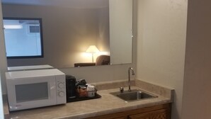 Una kitchenette compacta con microondas, pileta y muebles de madera.