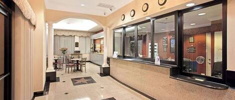 A hotel lobby with a reception desk, a dining area, and a hallway leading to other rooms.
