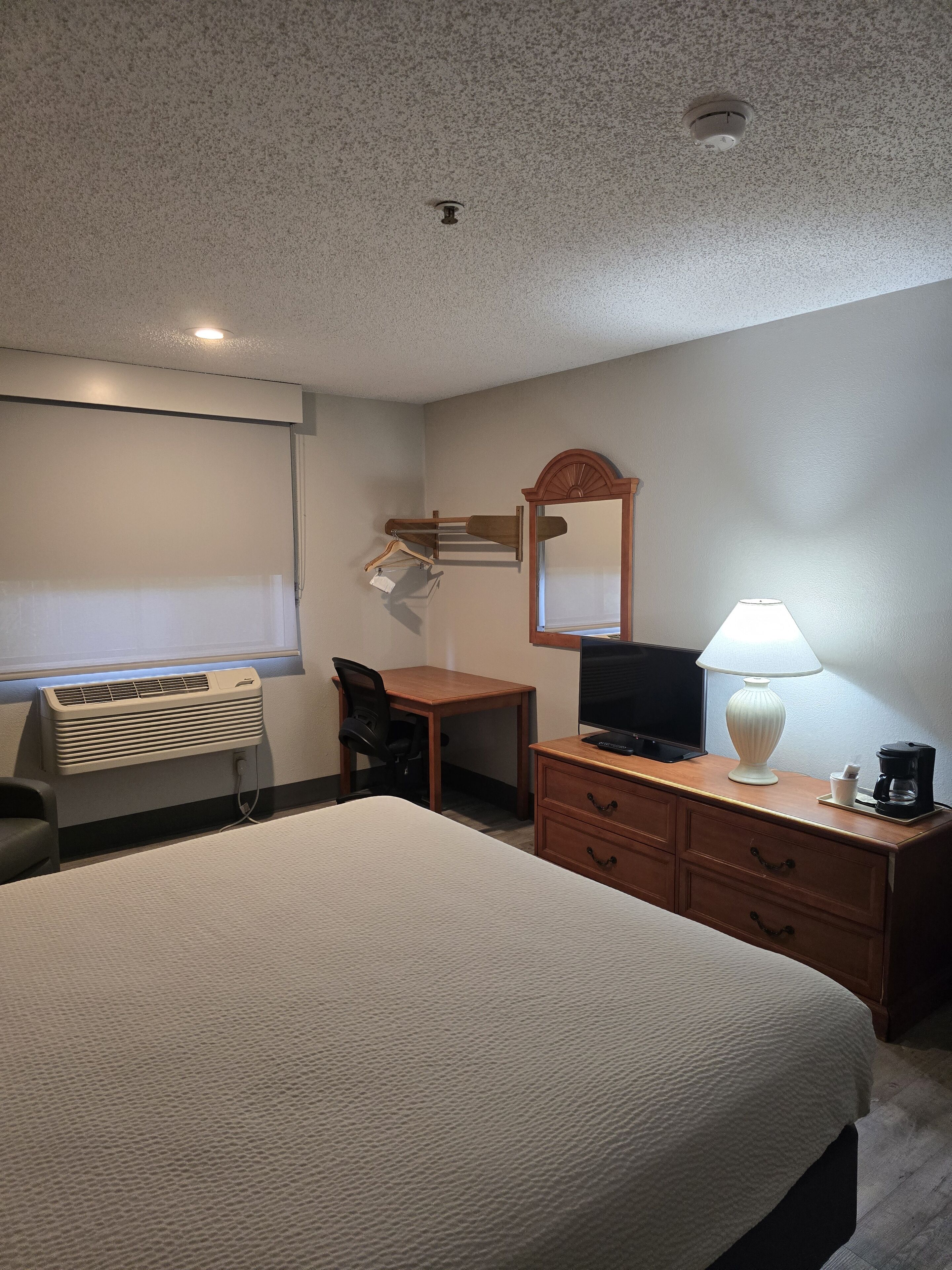 Quarto de hotel com cama, escrivaninha, cadeira, televisão, luminária e espelho.