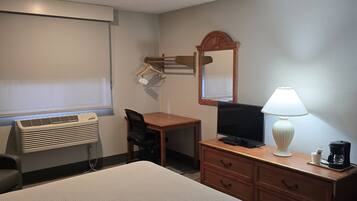 Una habitación de hotel con cama, escritorio, silla, televisor, lámpara y espejo.