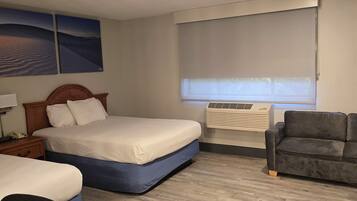 Quarto de hotel com cama de casal, escrivaninha com cadeira, sofá, janela com persianas e iluminação embutida no teto.