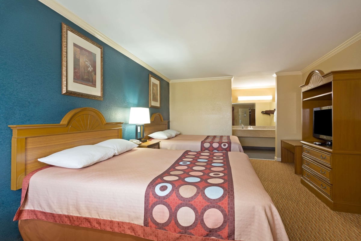 A hotel room with two beds, a TV, a dresser, and a bathroom visible in the background.
