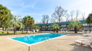 A swimming pool with lounge chairs and palm trees, surrounded by a building with a green roof. - Port Allen Inn (Port Allen)