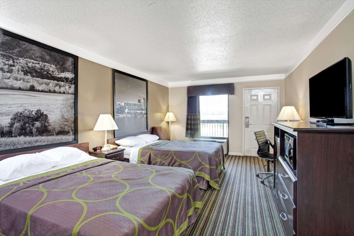 A hotel room with two beds, a television, a desk, and a window with a view of a building.
