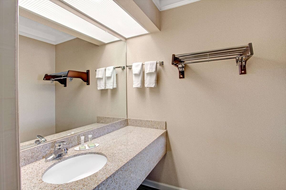 A bathroom with a granite countertop sink, a mirror, and a towel rack.