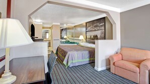 A hotel room with a bed, a desk, a chair, a lamp, a painting, and a view of another room. - Super 8 by Wyndham Knoxville East (Knoxville)