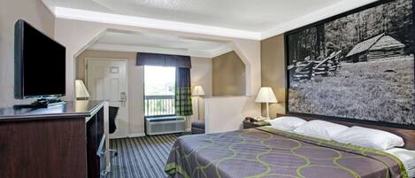 A hotel room with a large bed, a desk with a flat-screen TV, a window with a view of the outdoors, and a painting on the wall.
