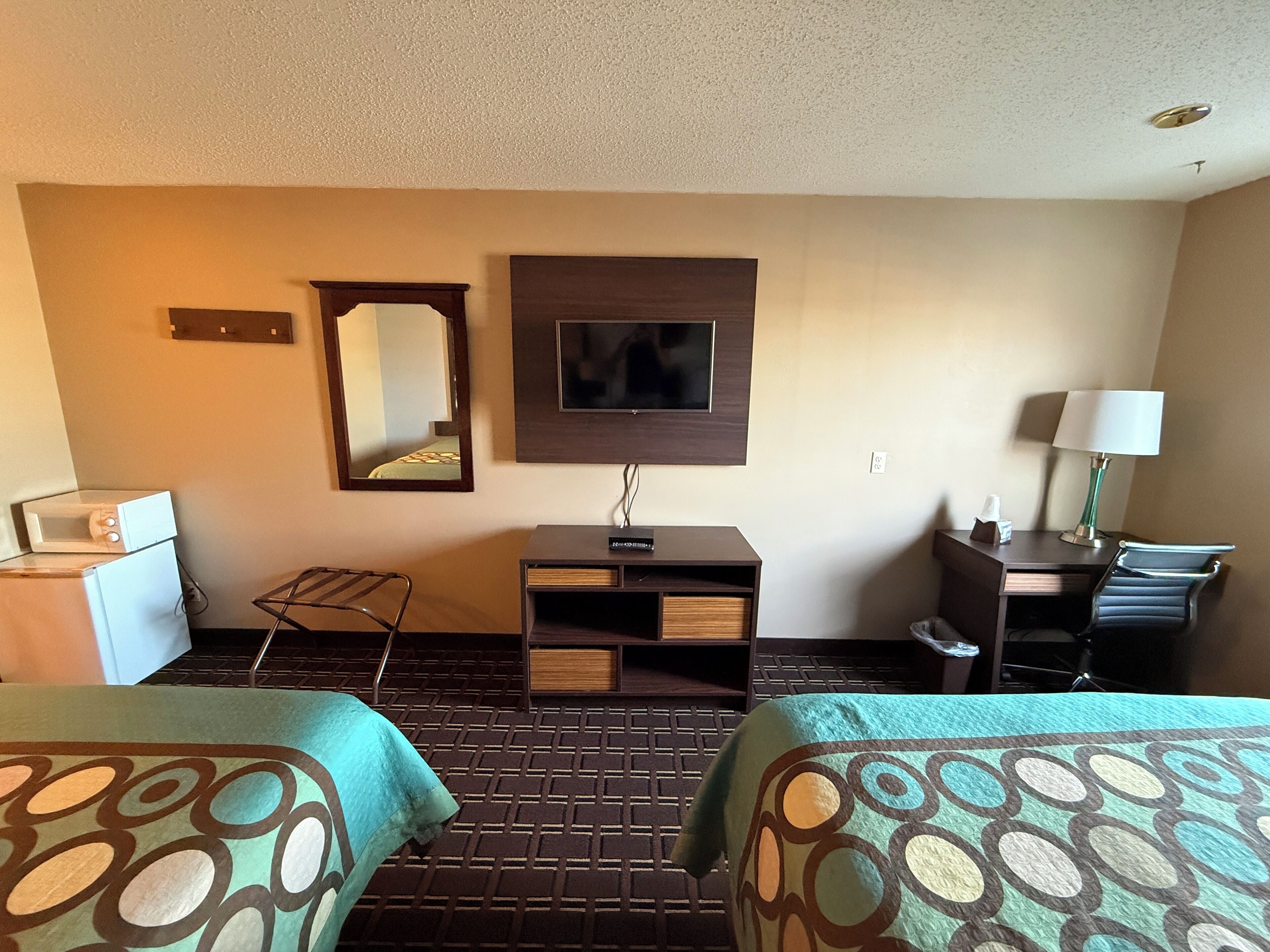 A hotel room with two beds, a desk with a lamp, a TV, a microwave, and a small seating area.