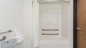 A bathroom with a shower, grab bars, a towel rack, and a wheelchair-accessible bench.