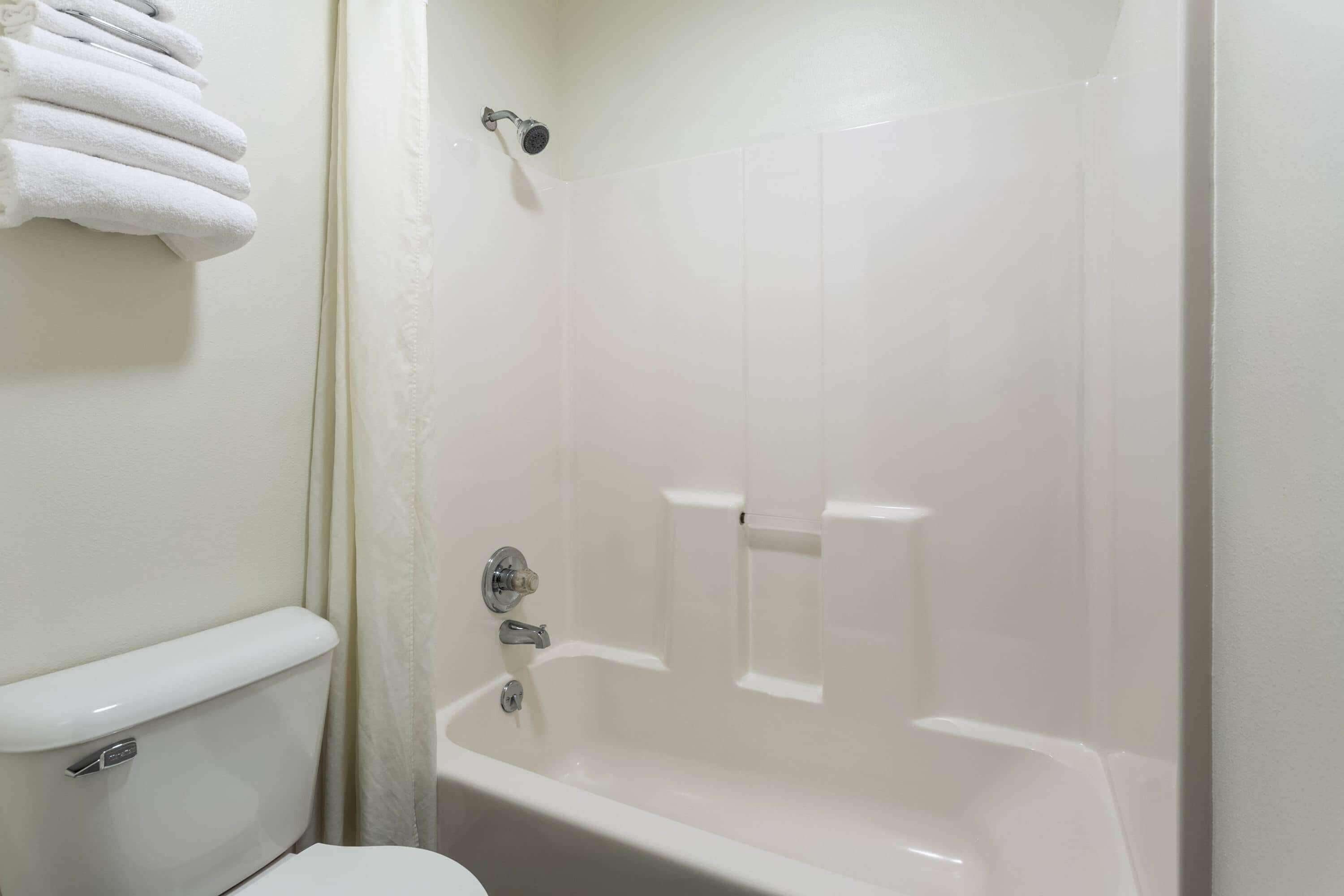 A bathroom with a white bathtub, a toilet, and a towel rack with folded towels.