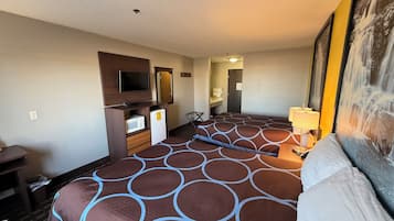 Relax in a spacious room with a large bed, flat-screen TV, and a dresser housing a microwave and refrigerator.