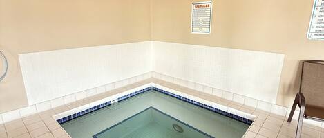 A swimming pool with a tiled floor and a wooden ceiling. There are two metal ladders leading into the pool. A sign with 'SPA RULES' is visible on the wall.
