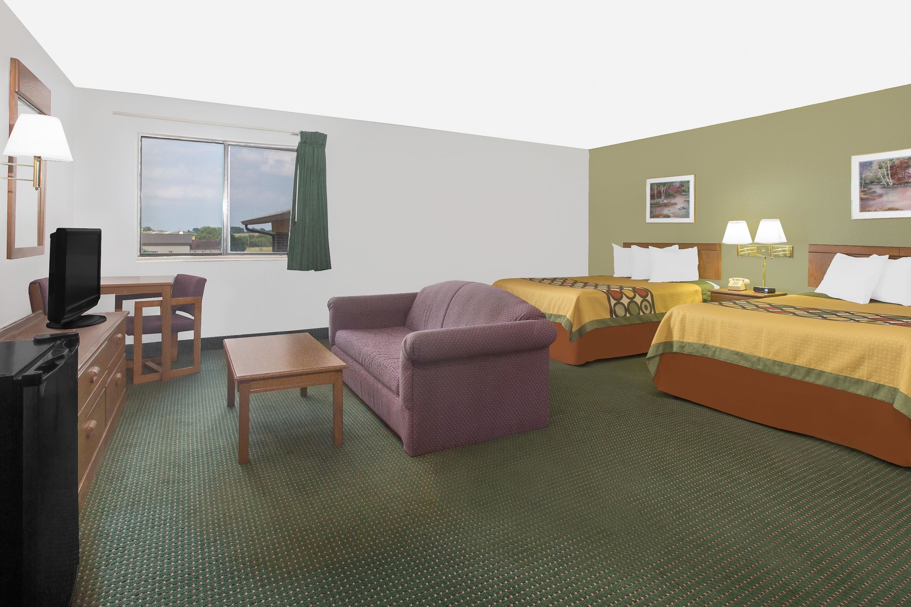 A hotel room with a sofa, two beds, a desk, a television, and a window with a view of buildings.