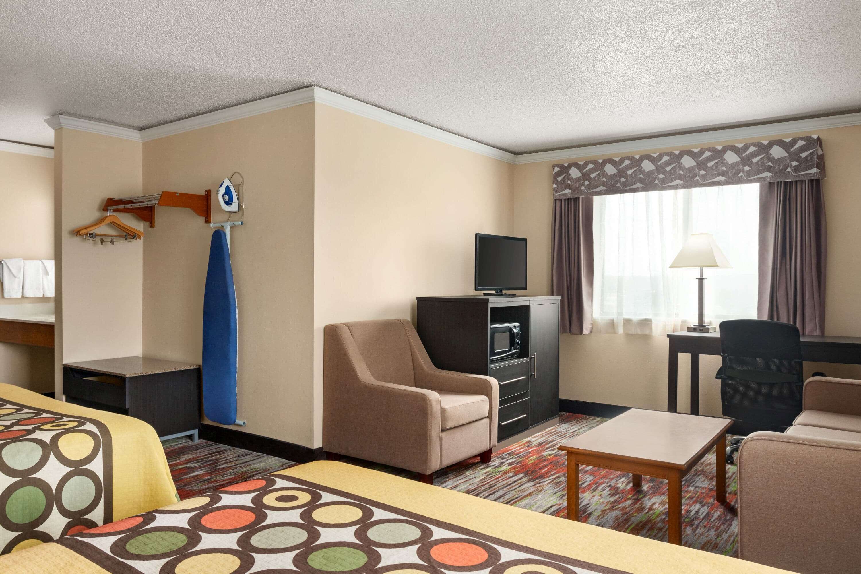 A hotel room with a bed, a desk, a chair, a television, and a wardrobe.