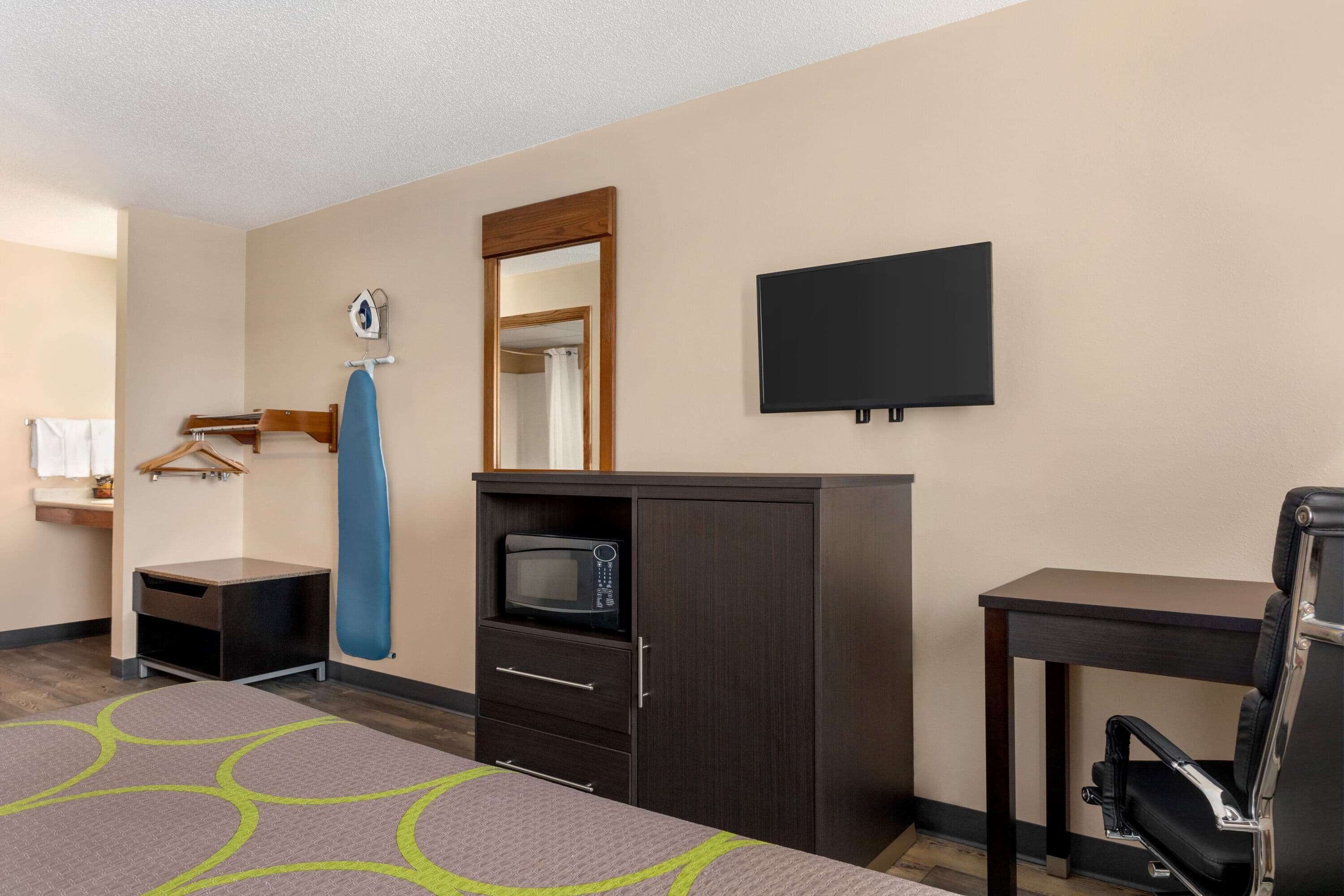 Hotelkamer met een bed, bureau, stoel, televisie, magnetron, kast en spiegel.