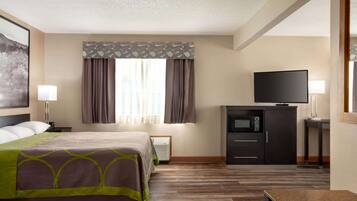 A hotel room with a bed, a flat-screen TV, a microwave, and a desk with a lamp.