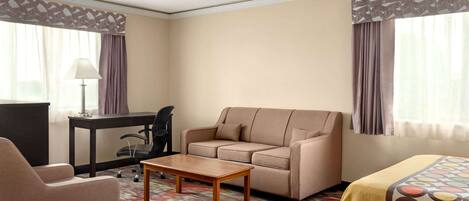 A hotel room with a sofa, armchair, desk, and a bed with a patterned bedspread.