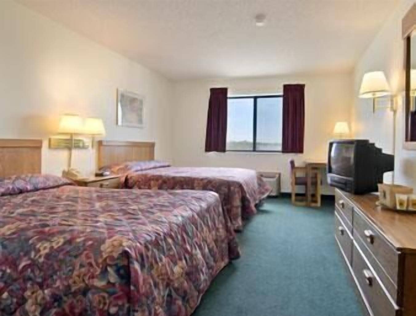 Une chambre d’hôtel avec deux lits, une télévision, un bureau et une fenêtre avec des rideaux.