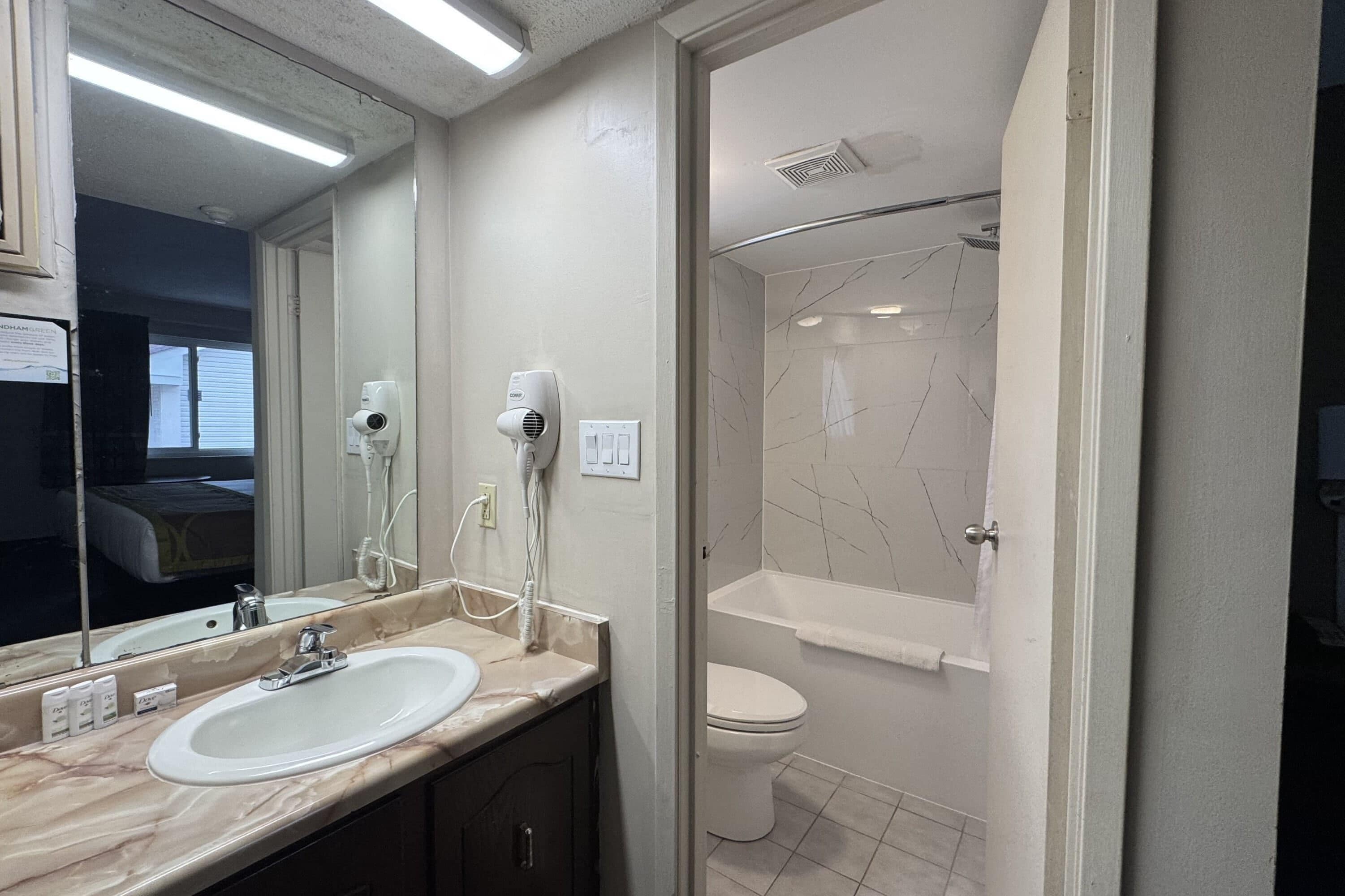 A bathroom with a sink, mirror, hairdryer, and a shower area.