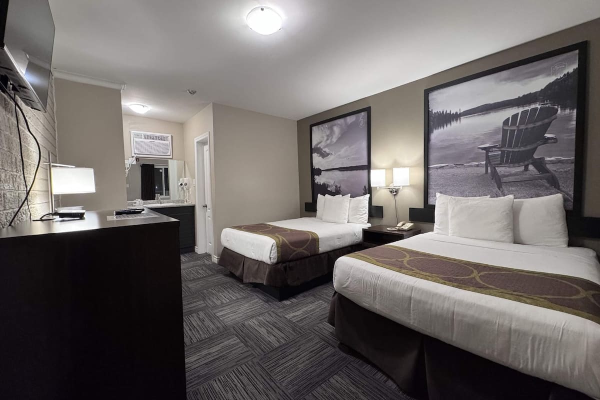 Una habitación de hotel con dos camas, un escritorio, una silla y un ventanal grande.