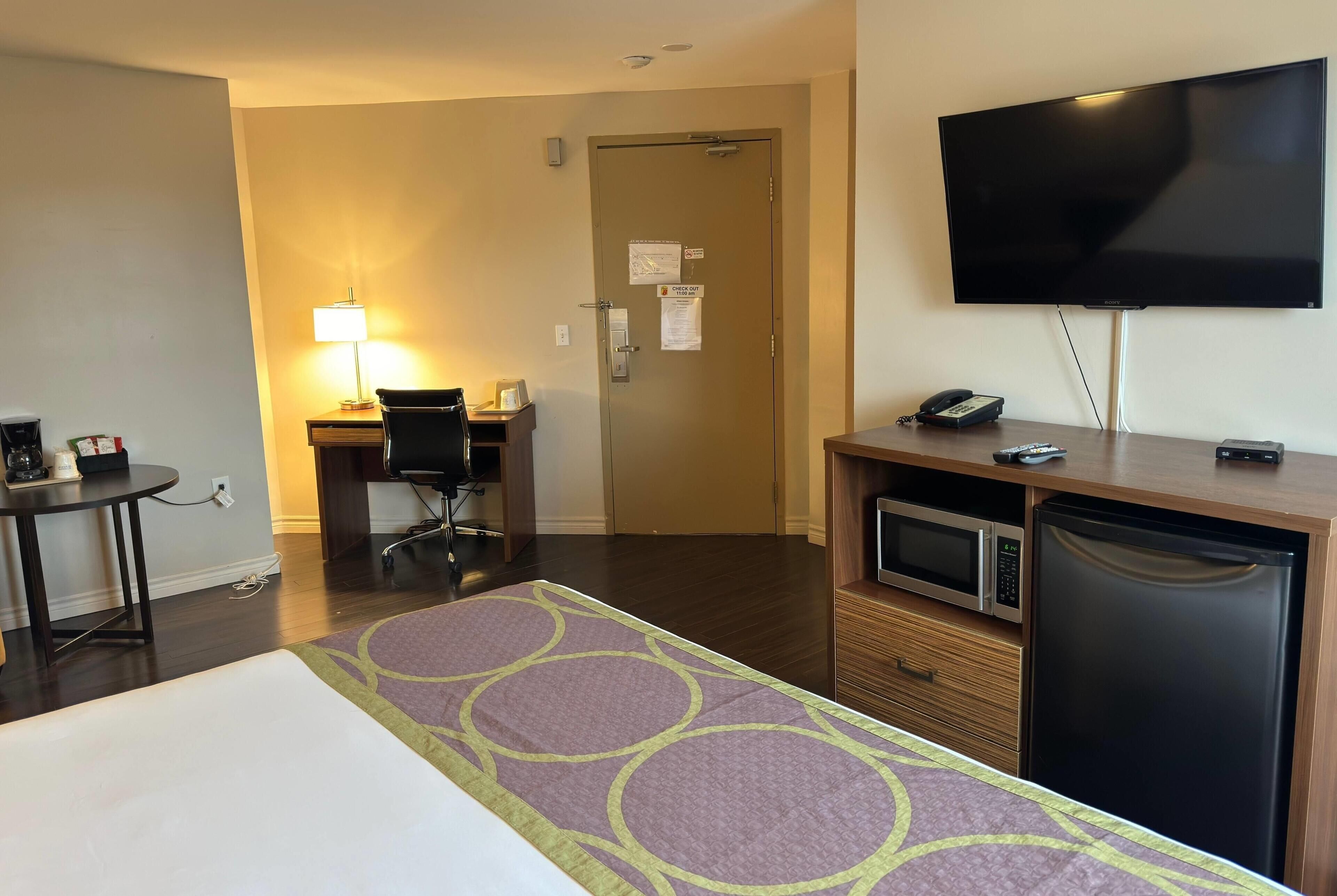 A hotel room with a bed, a desk with a chair, a television, a microwave, and a refrigerator.