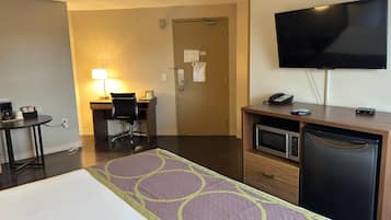 A hotel room with a bed, a desk with a chair, a television, a microwave, and a refrigerator.