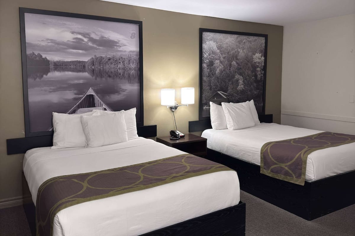 Habitación de hotel con dos camas, una mesita de noche con lámpara y dos cuadros grandes en la pared.