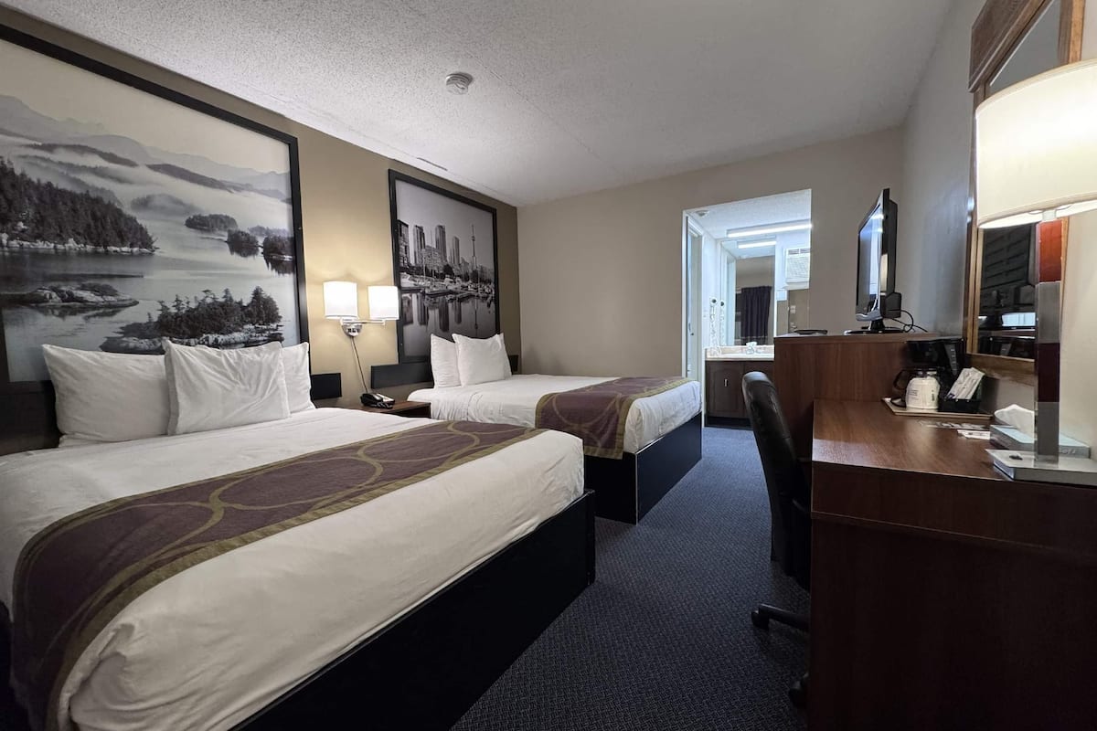 Una habitación de hotel con dos camas, un escritorio con computadora, una silla y un espejo grande.
