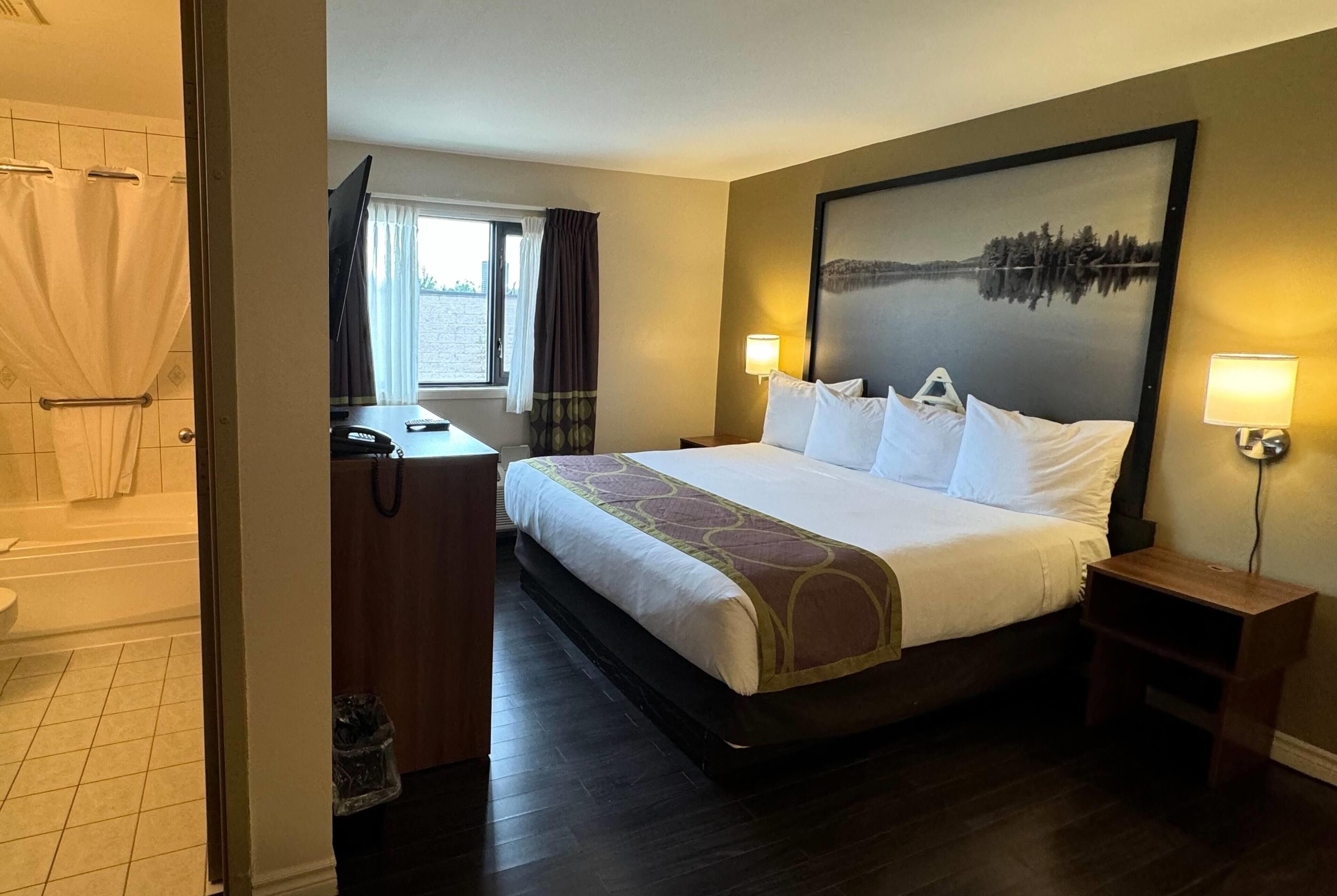 A hotel room with a large bed, a bathroom with a bathtub, a desk with a chair, and a window with curtains.