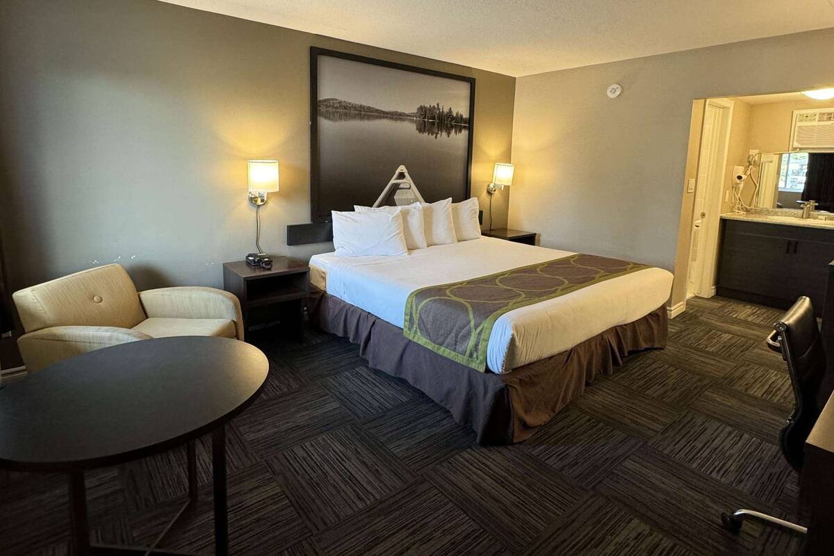 Habitación de hotel con cama, dos mesitas de noche, una silla, una mesita pequeña y un cuadro en la pared.
