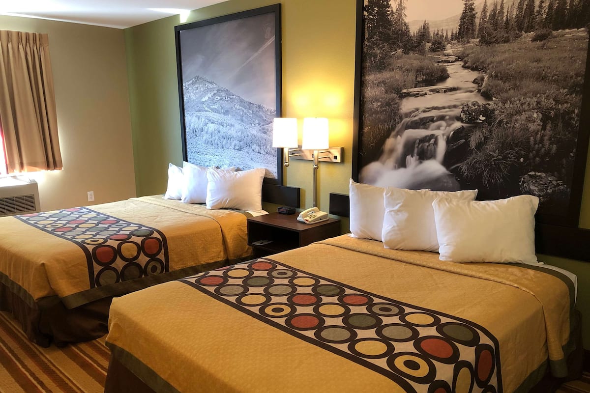 Une chambre d’hôtel avec deux lits, chacun recouvert d’une couvre-lit à motifs, une table de chevet avec une lampe et un grand tableau encadré représentant un paysage montagneux.