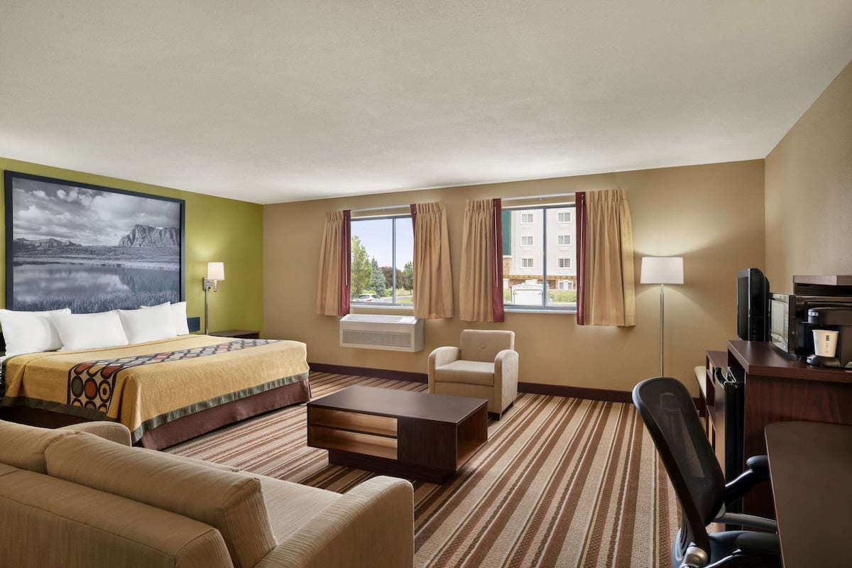 Une chambre d’hôtel comprenant un lit, un bureau, une chaise, un canapé et une grande fenêtre avec des rideaux.