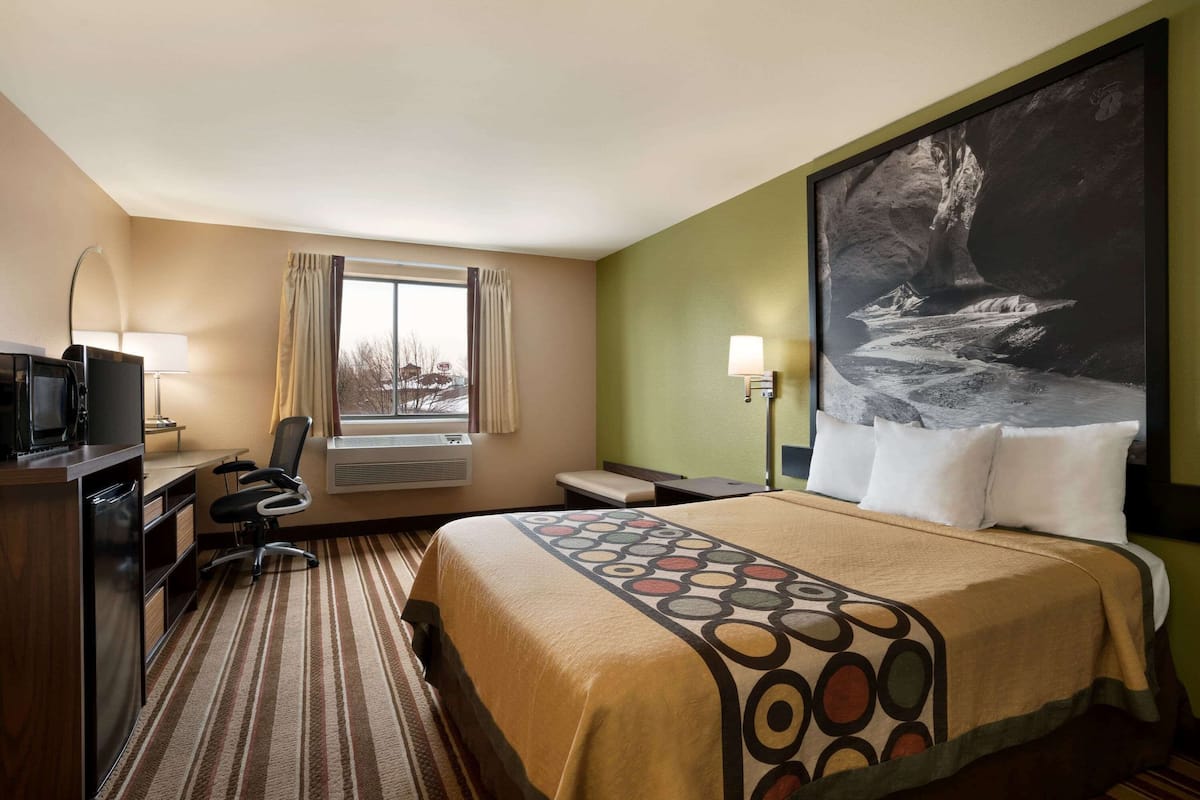 Une chambre d’hôtel avec un grand lit, un bureau avec une chaise, une télévision et une fenêtre avec des rideaux.