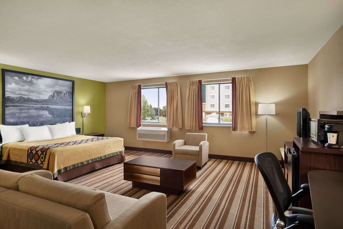 Une chambre d’hôtel avec un lit, un bureau, une chaise, un canapé et une grande fenêtre avec des rideaux.