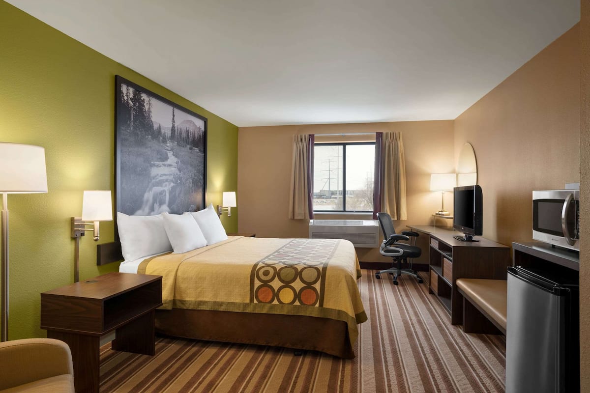 Une chambre d’hôtel équipée d’un lit, d’un bureau, d’une chaise, d’une télévision et d’une grande fenêtre.