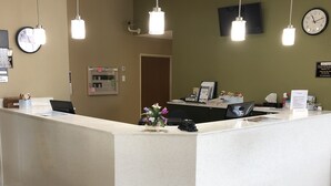 A reception area with a white counter, hanging pendant lights, a clock, and a wall-mounted information board. - Super 8 by Wyndham S Jordan/Sandy/Slc Area (South Jordan)