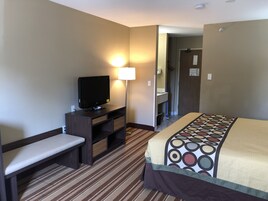 Habitación de hotel con una cama, un televisor sobre un mueble de madera, una mesita de noche, una lámpara y una alfombra a rayas.