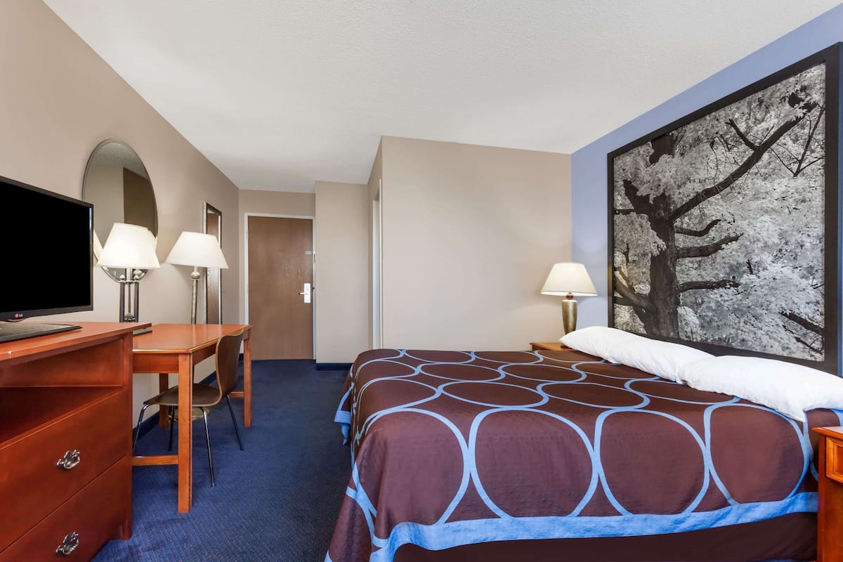 A hotel room with a bed, desk, TV, and two lamps.