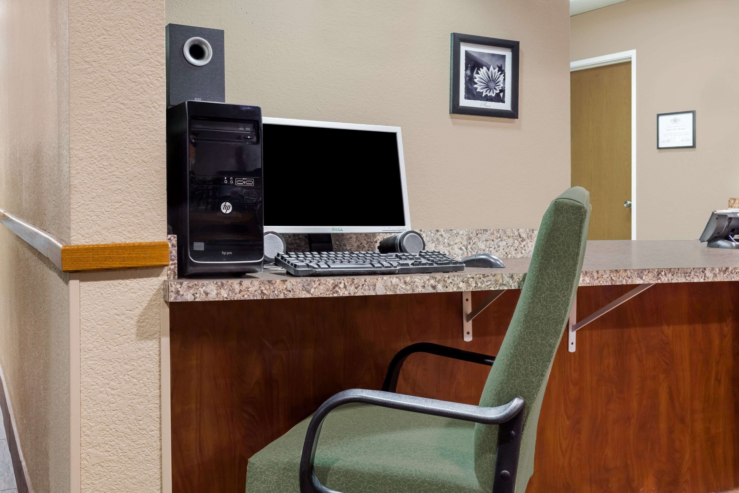 A hotel reception desk with a desktop computer, a green chair, and a framed picture on the wall.