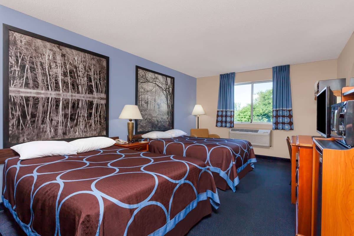 A hotel room with two beds, a TV, a desk, and a large window with curtains.