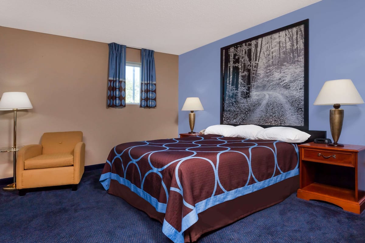 A hotel room with a large bed, two bedside tables with lamps, a chair, and a large painting on the wall.