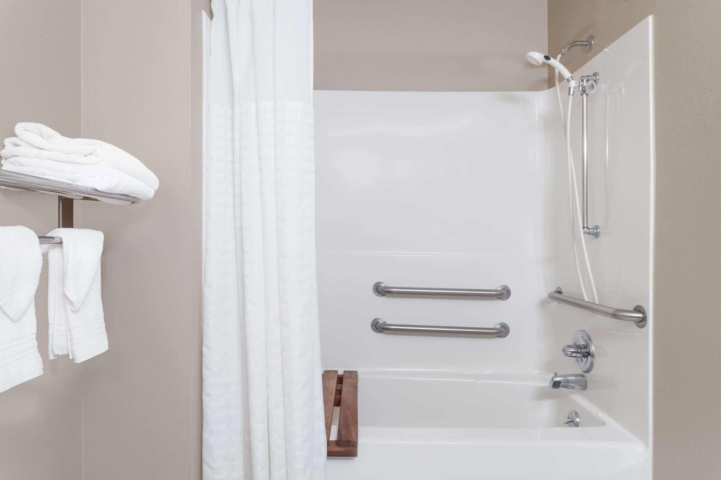 A modern bathroom with a bathtub, shower, and handrails.