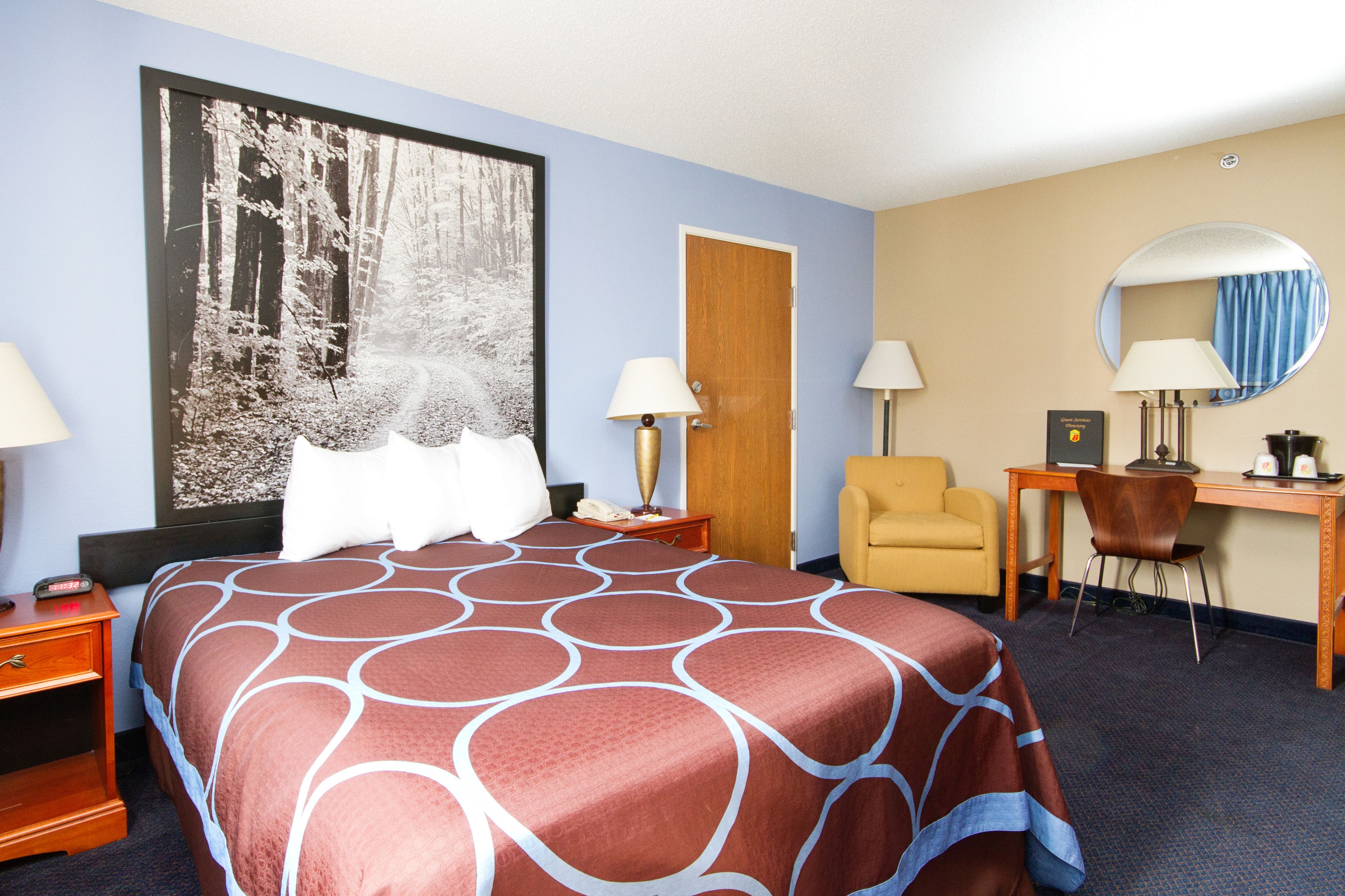 A hotel room with a large bed, a desk, a chair, a mirror, and a painting on the wall.