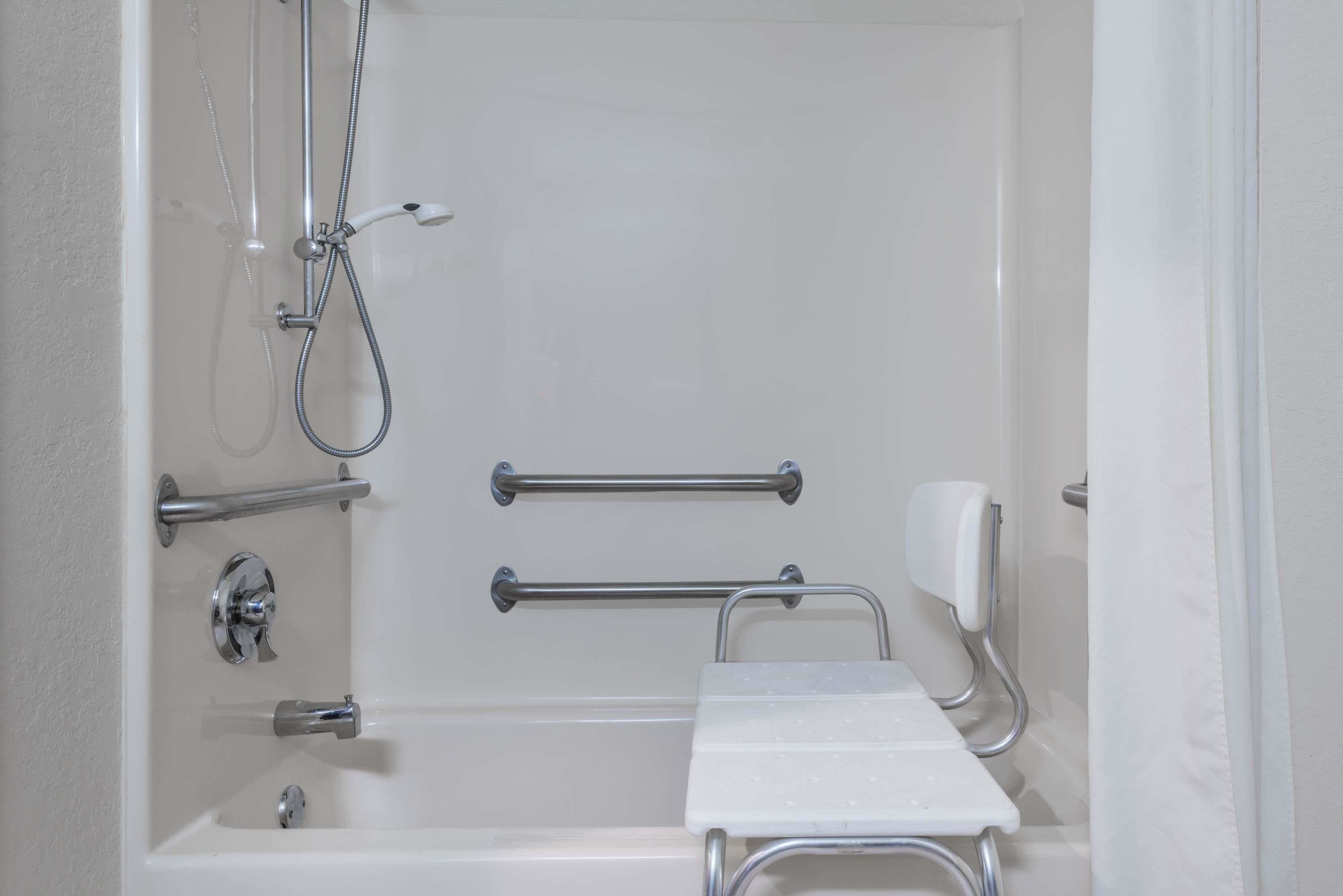 A white bathtub with a handheld showerhead, grab bars, and a handheld soap dispenser.